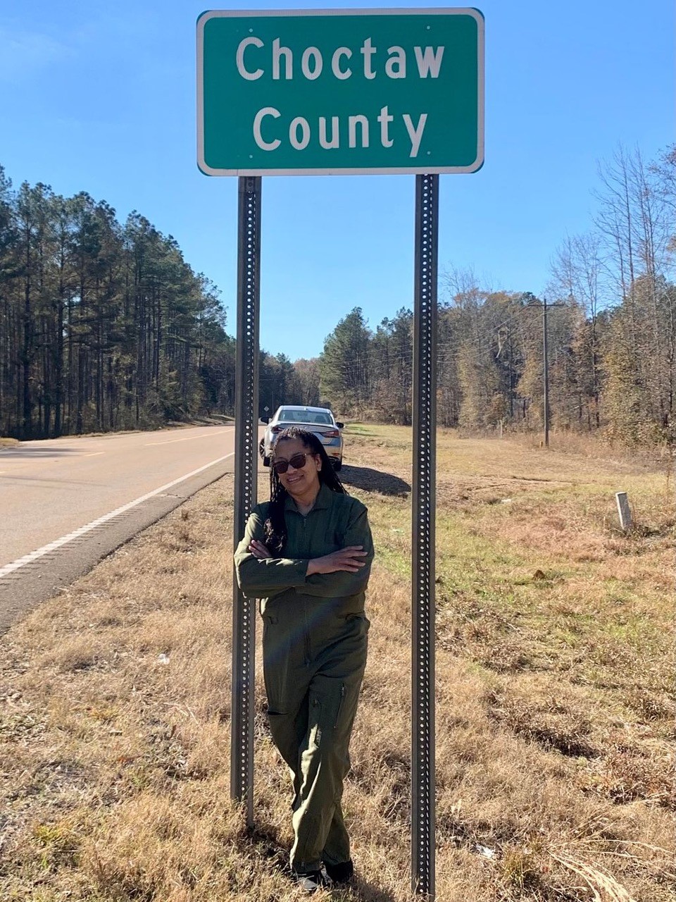 Black woman stands in front of Chocktaw County green highway sign