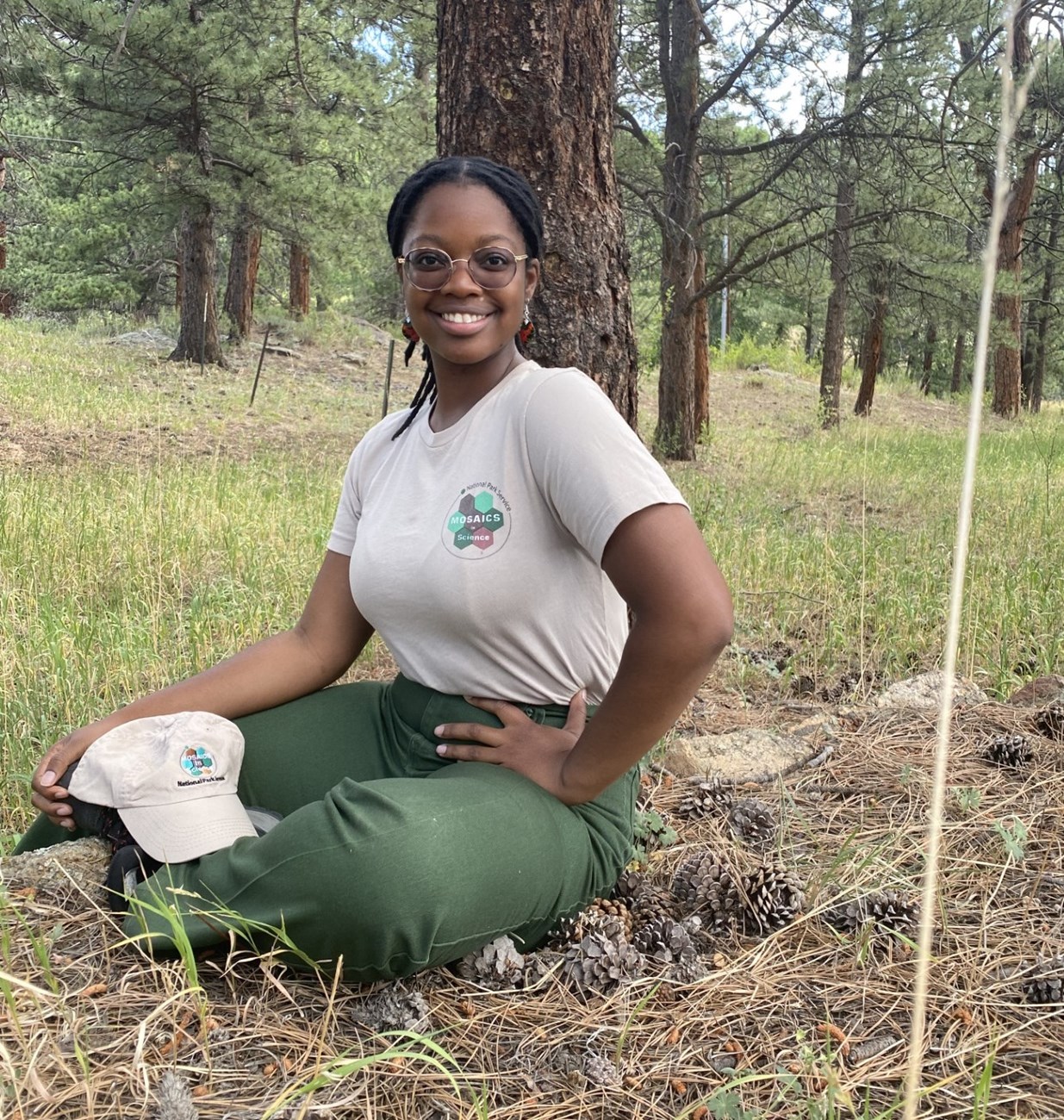 Tonya under a tree A young woman wearing a tan shirt with a logo that reads "Mosaics in Science" sits under a tree