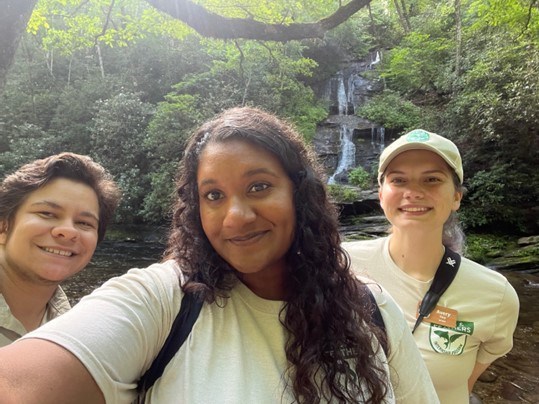 Two young woman and one man smile for a selfie in nature