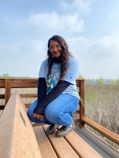 A young woman poses for a photo kneeling down on a dock