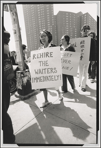 An Asian American woman holds a picket sign with text Rehire the Workers Immediately