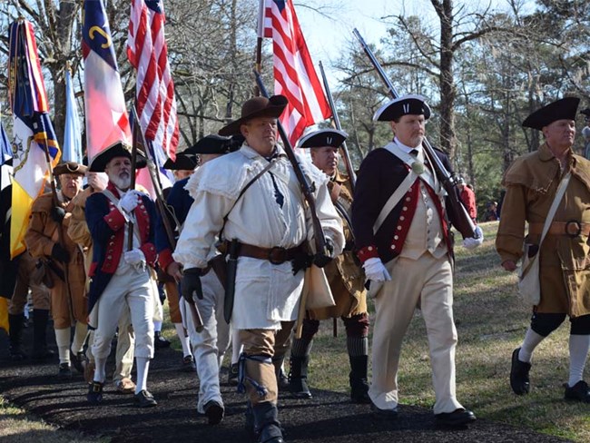 Revolutionary War reenactors march with flags Revolutionary War reenactors march with flags