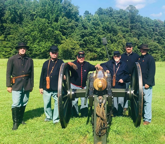 6 living historians dressed as Federal soldiers pose next to a cannon.
