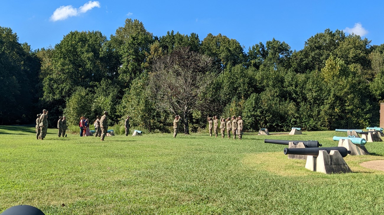 7 soldiers with right arms raised taking an otath stand in front of a crowd of 14 people.