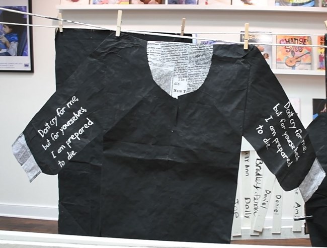 A black paper shirt with newsprint in the neck hole and cuffs - quotes printed on both sleeves.