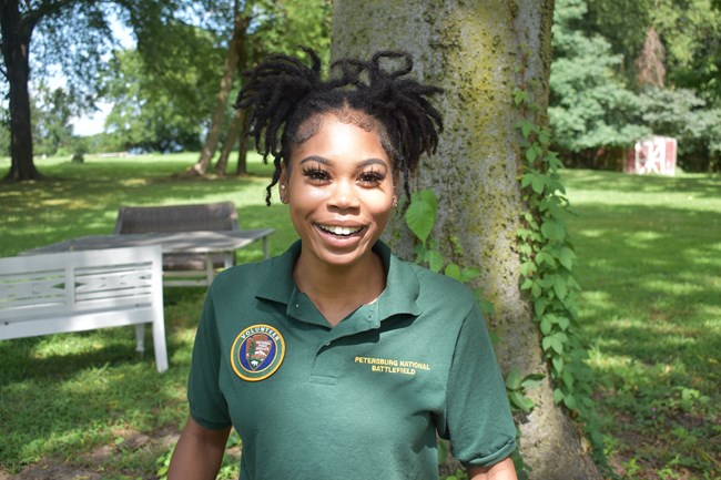 A black woman with her hair pulled back wearing a green NPS volunteer polo shirt.