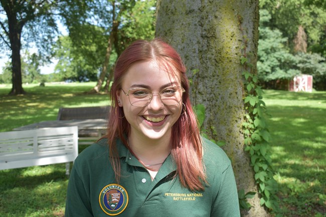 A white woman with long red hair wearing a green NPS Volunteer polo style shirt,