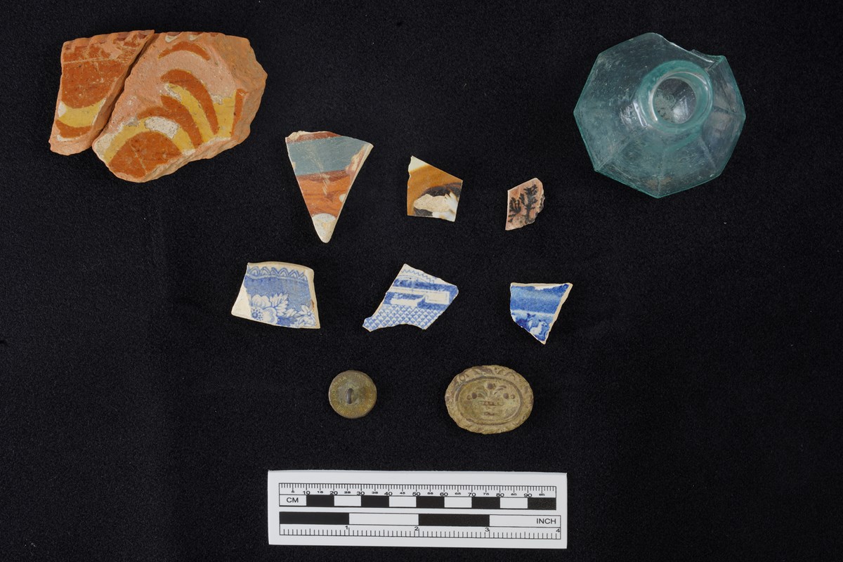 A black background with eleven artifacts displayed. Pieces of pottery, a glass bottle, a button, and an unknown object.