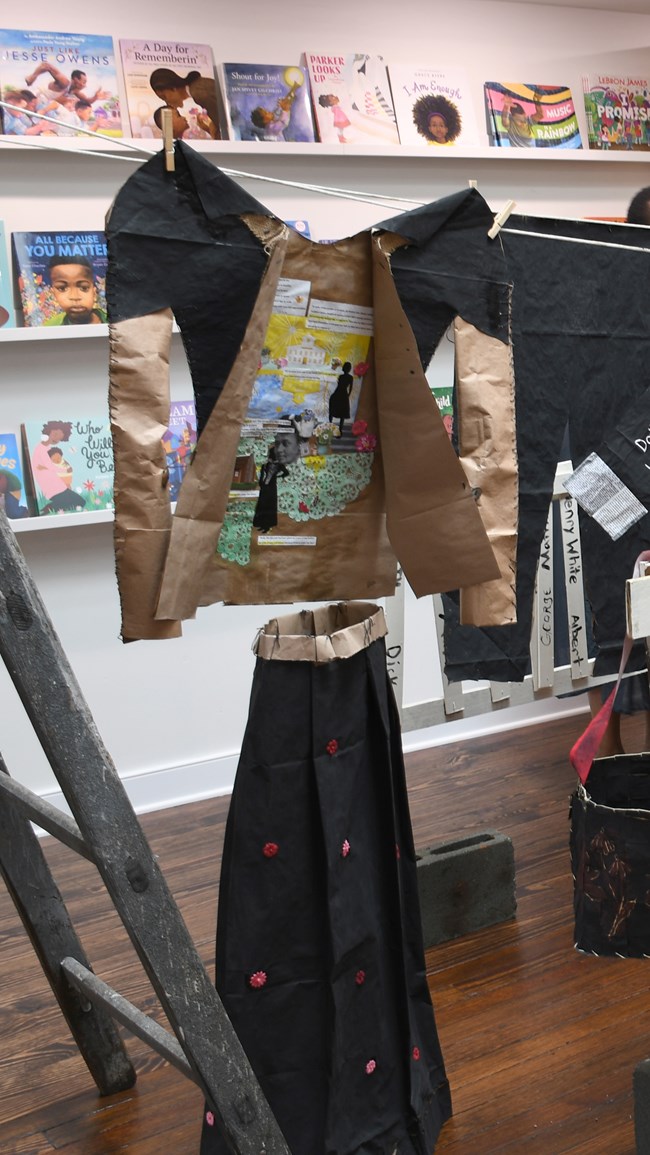 A paper shirt painter black with a colorful interior hangs above a paper skirt painted black.