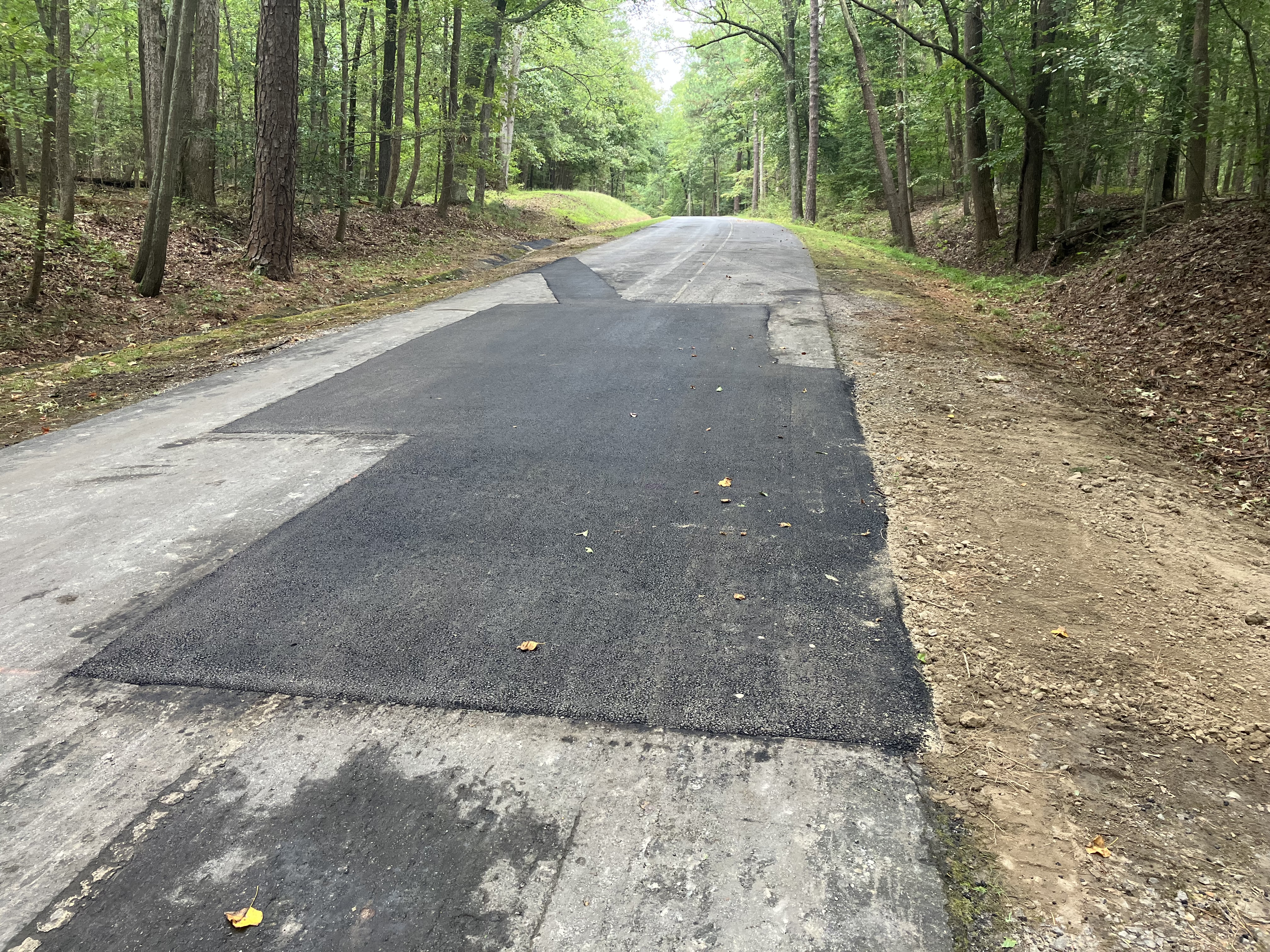 A large patch of dark black asphalt in the middle of and arcoss a single lane road.
