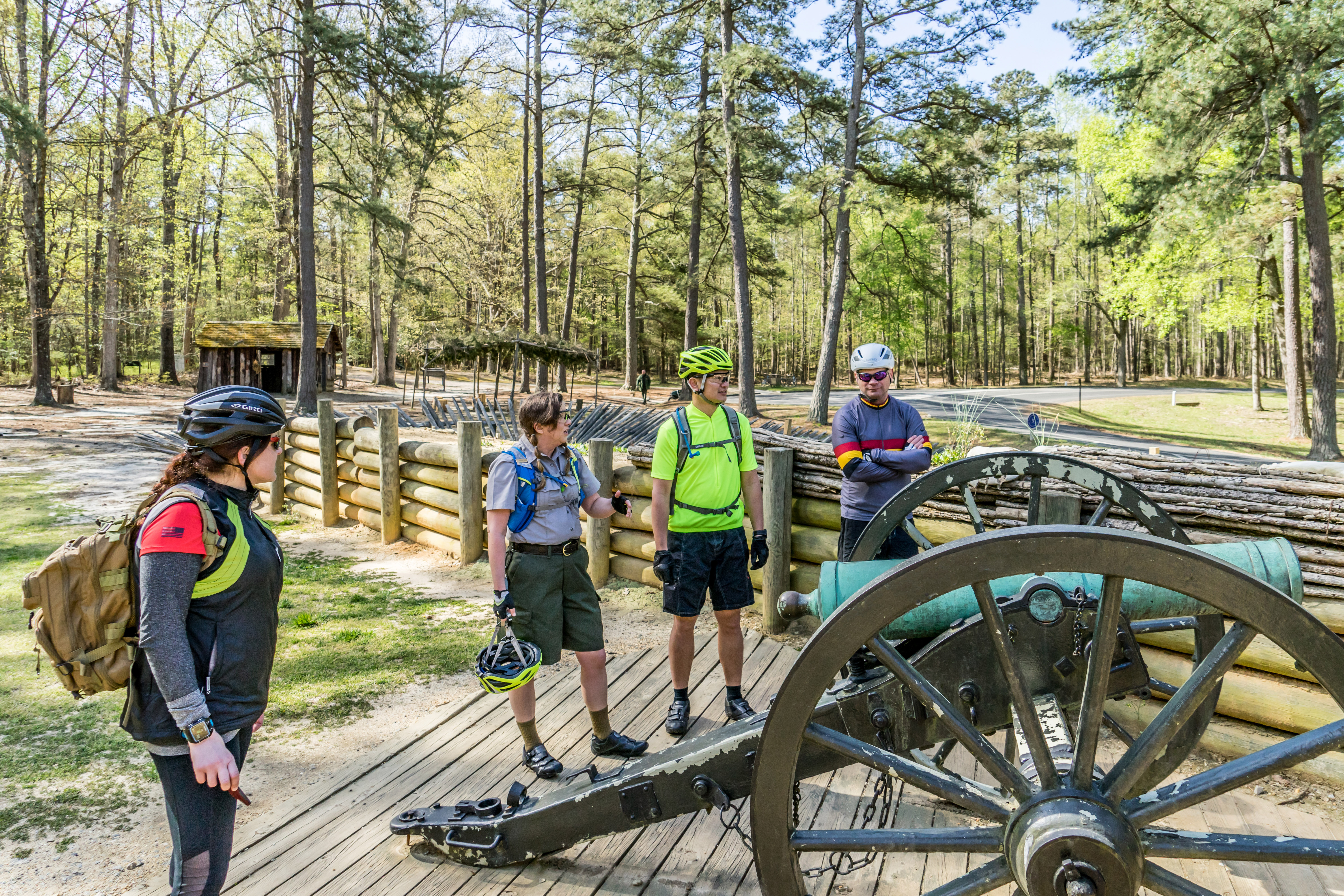 Biking in Battlefield LR One Ranger and three visitors wearing bike helmets and backpacks stand around a green patina cannon.