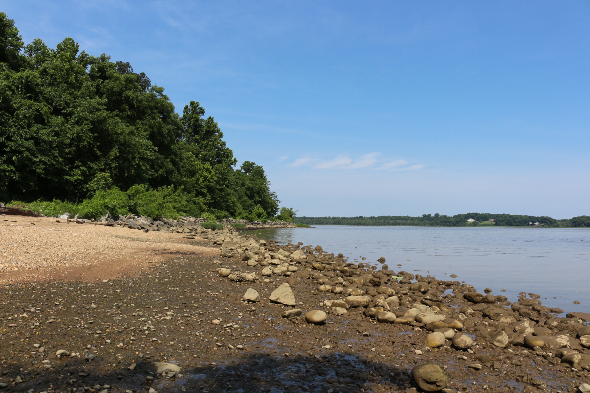 Rock covered shoreline with trees on the left and water on the right.