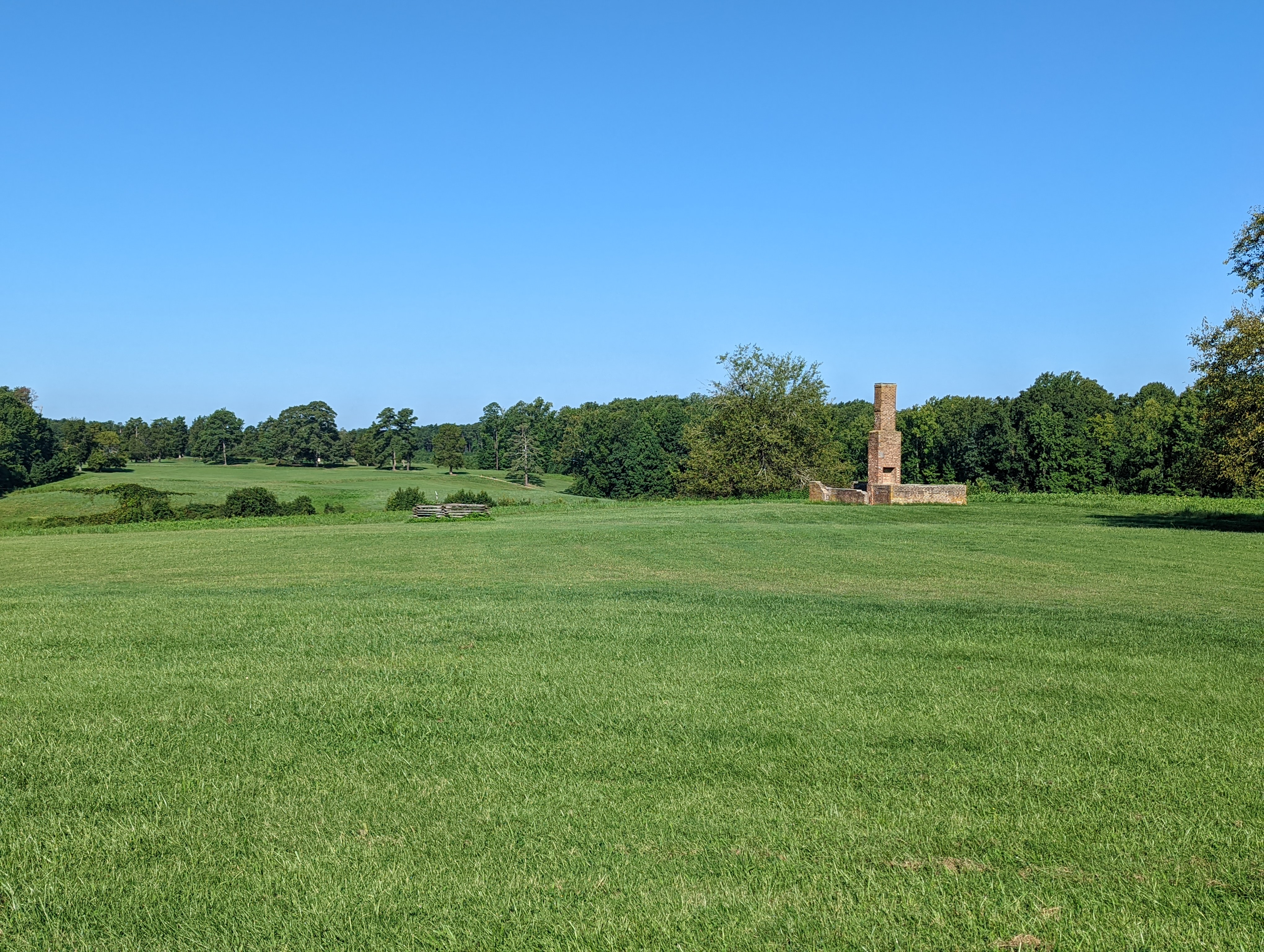 View from Fort Morton toward the Crater Large mowed green field with a brick chimney and low brick wall on the right with second large mowed field in the distance.