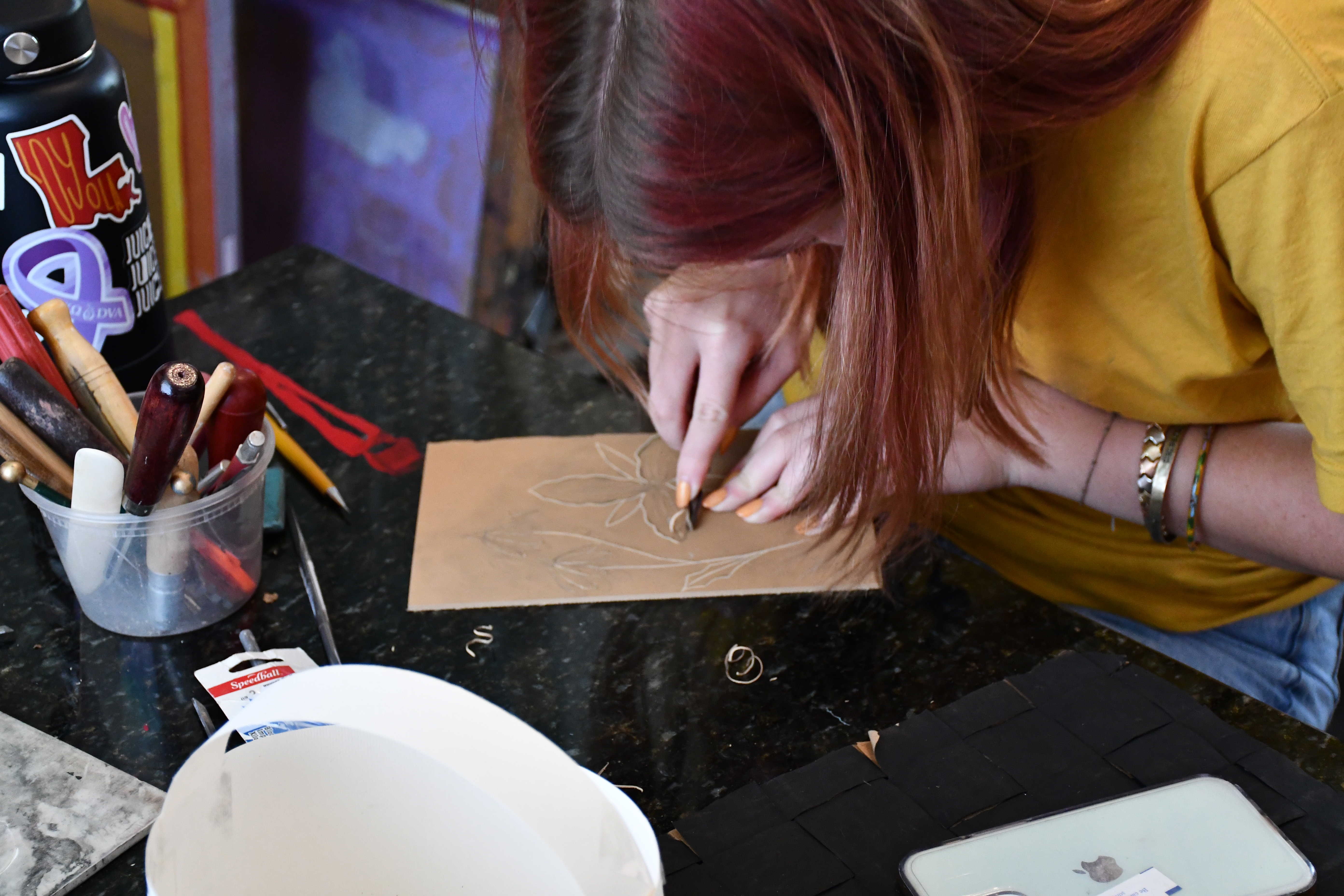 A female carves the shape of a plants on a board.