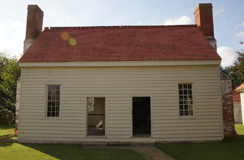 Appomattox Plantation kitchen building Side view of a white single-story building with two doors toward the middle and a single window between the doors and the edge of the building. The structure has a red roof and a red brick chimney on bother ends.