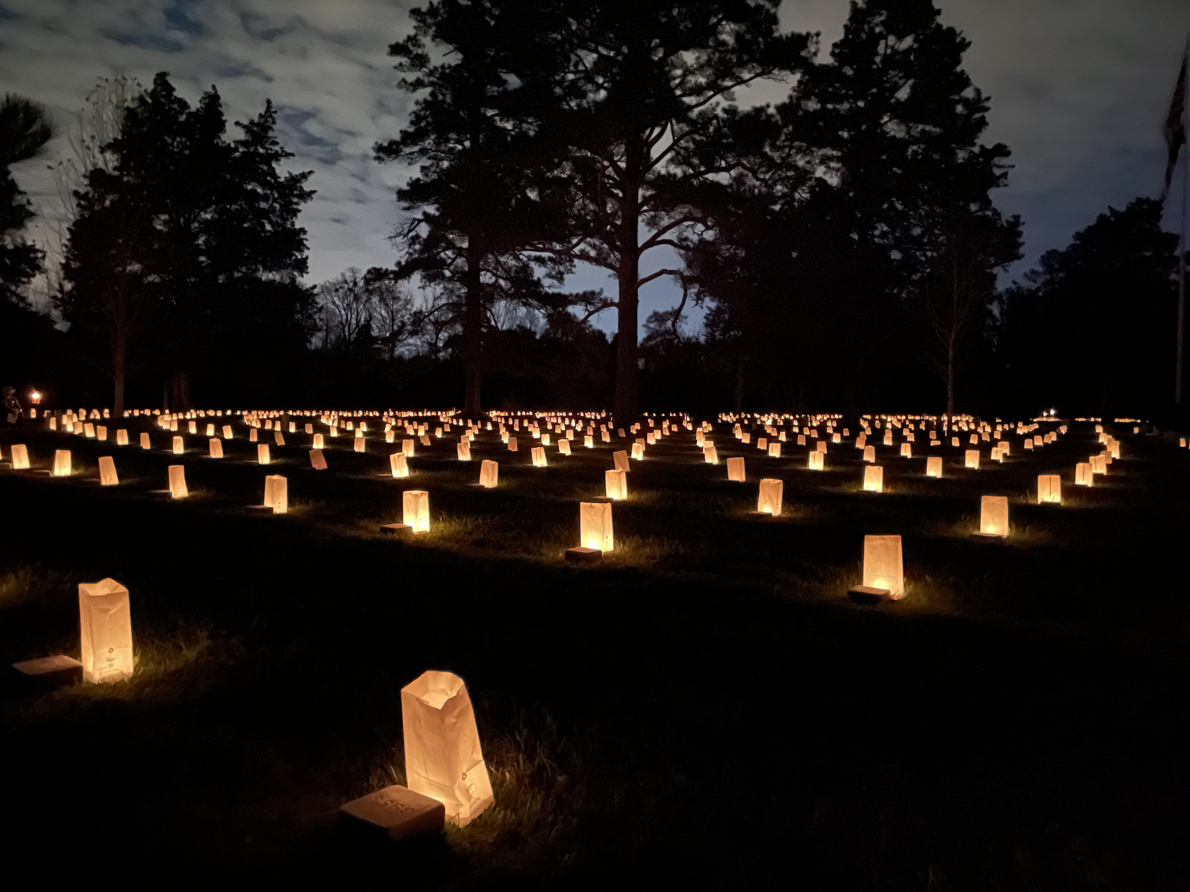 Hundreds of luminaries light grave markers at twilight.