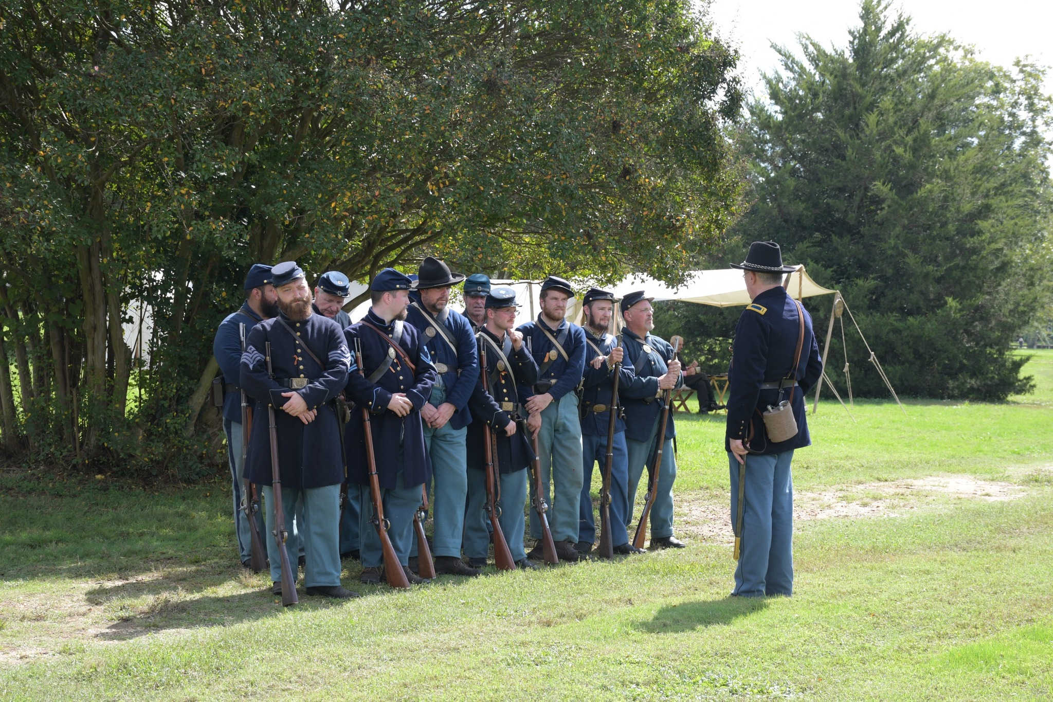 Union Soldiers in formation Tweleve man wearing US Civil War infantry uniforms stand in formations in front of a large shrub.