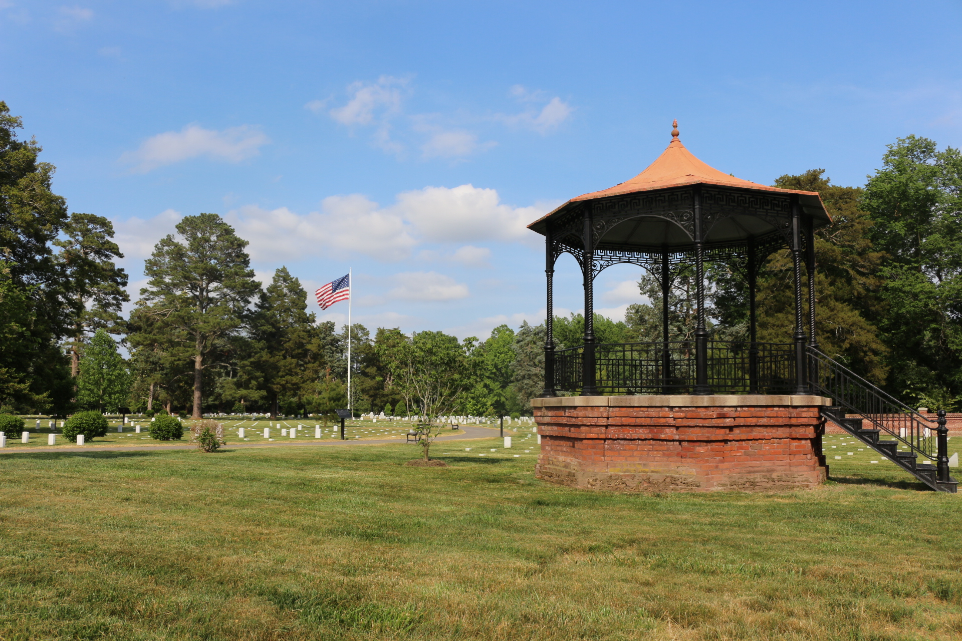 A brick rotunda in a grass field with white headstones in the background.
