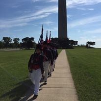 Photo of sailors walking and carrying muskets and flags with memorial column in background Photo of sailors walking and carrying muskets and flags with memorial column in background
