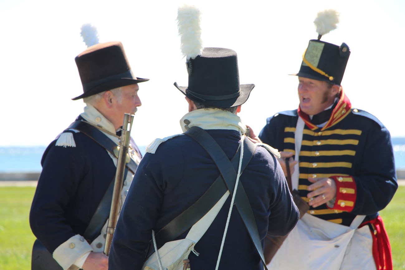 Three reenactors, circled together, confer before a demonstration.