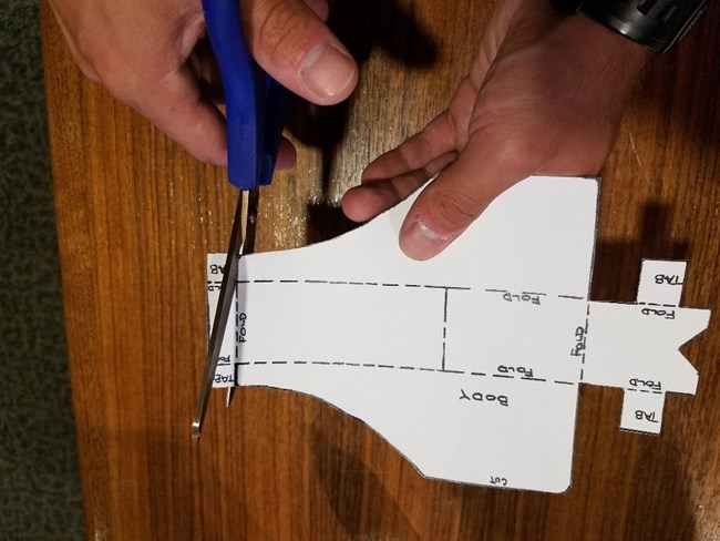 A pair of scissors makes a small cut in a cut out piece of paper to make a tab.