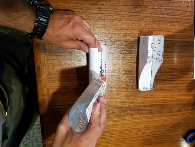 One hand holds a paper cylinder while the other glues the edge of the paper.