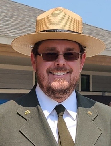 Head shot of Brian Harmon. He is wearing a NPS uniform which includes a green blazer and tie, white shirt and straw hat.