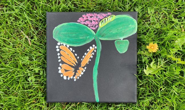 Painting of a butterfly and flower laying in the grass.