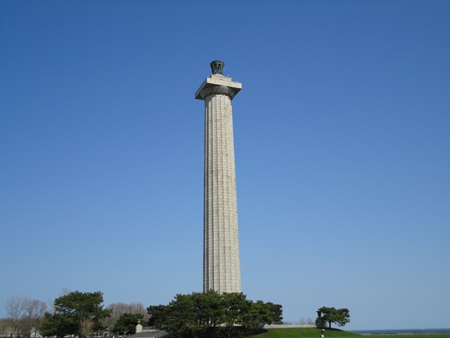 An architecturally designed, 352-foot tall, granite column with a fronze lantern on top  surrrounded by a true blue sky