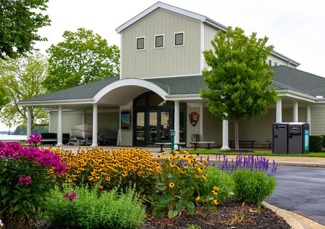 Out front of a light colored building with green roof and a 2nd story in the center is a bed of colorful annunals