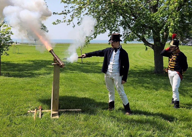 Two men in historic dress fire a small cannon.
