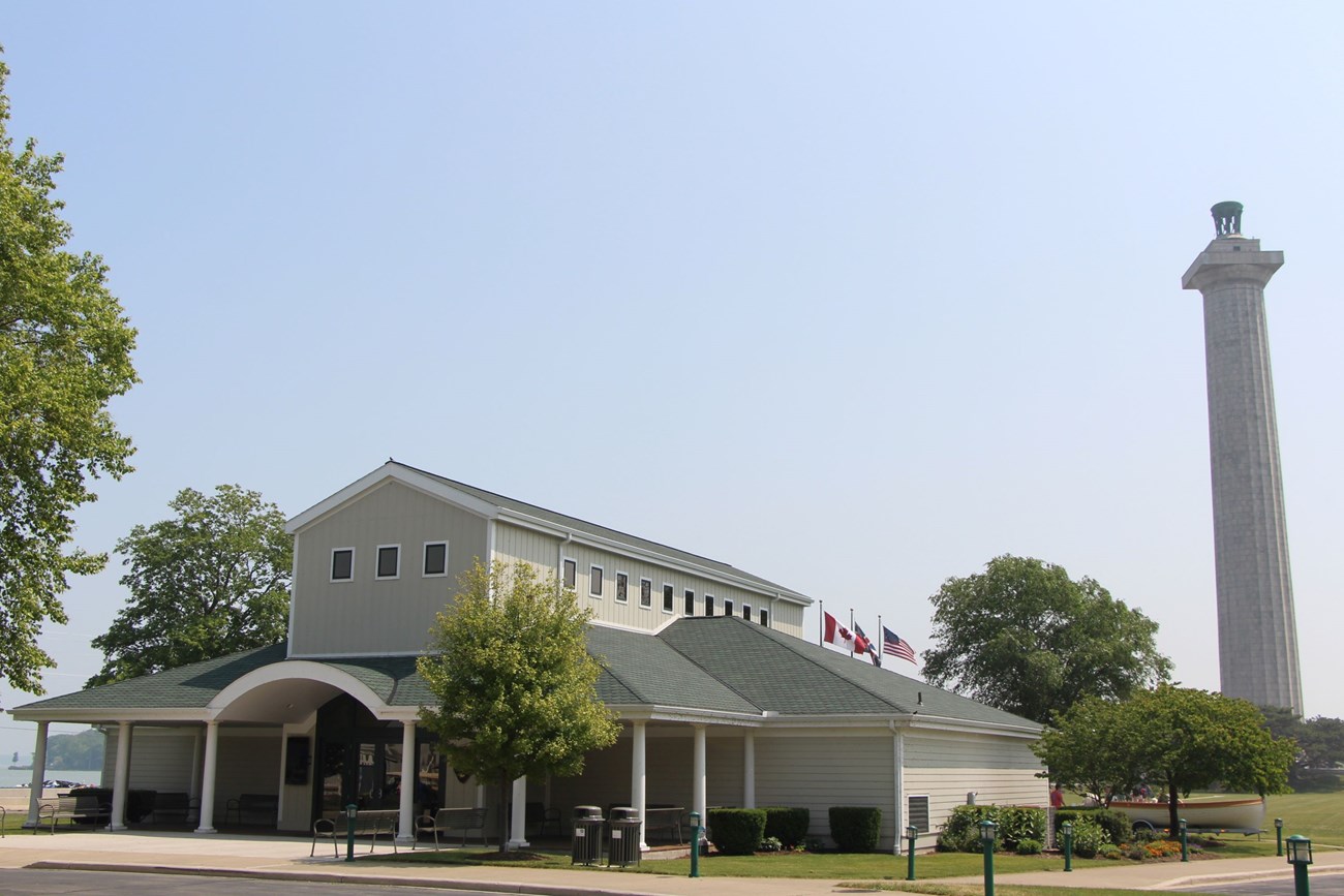 a green roofed one story building with a second story in the center, three flags behind and a tall stone memorial column