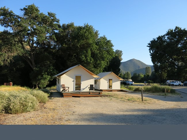 The front view of a canvas-sided tent cabin with a screen door and two Adirondack style chairs on the front porch.