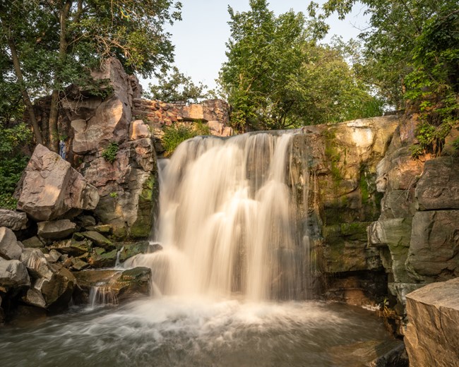 A waterfall plunges over reddish rock in warm light.