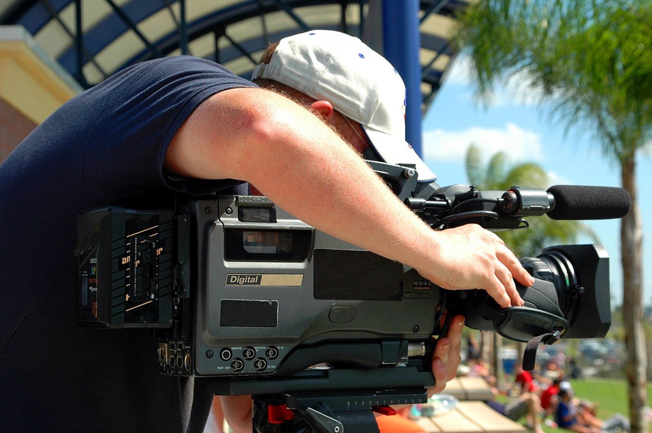 A man outside with a large camera for filming