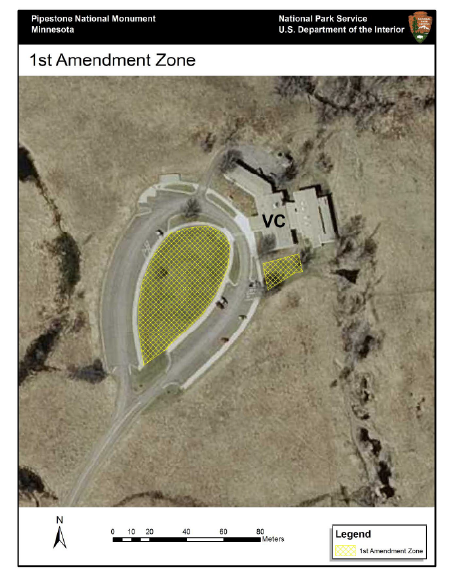 A bird's eye view of a traffic circle. The road comes from the south and describes a oval. The interior space is layered with a yellow crosshatch denoting the 1st amendment area. An additional such area lies to the east.