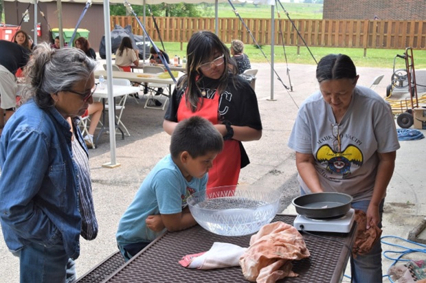 4 people outside at a picnic table over a bowl and hot pot.