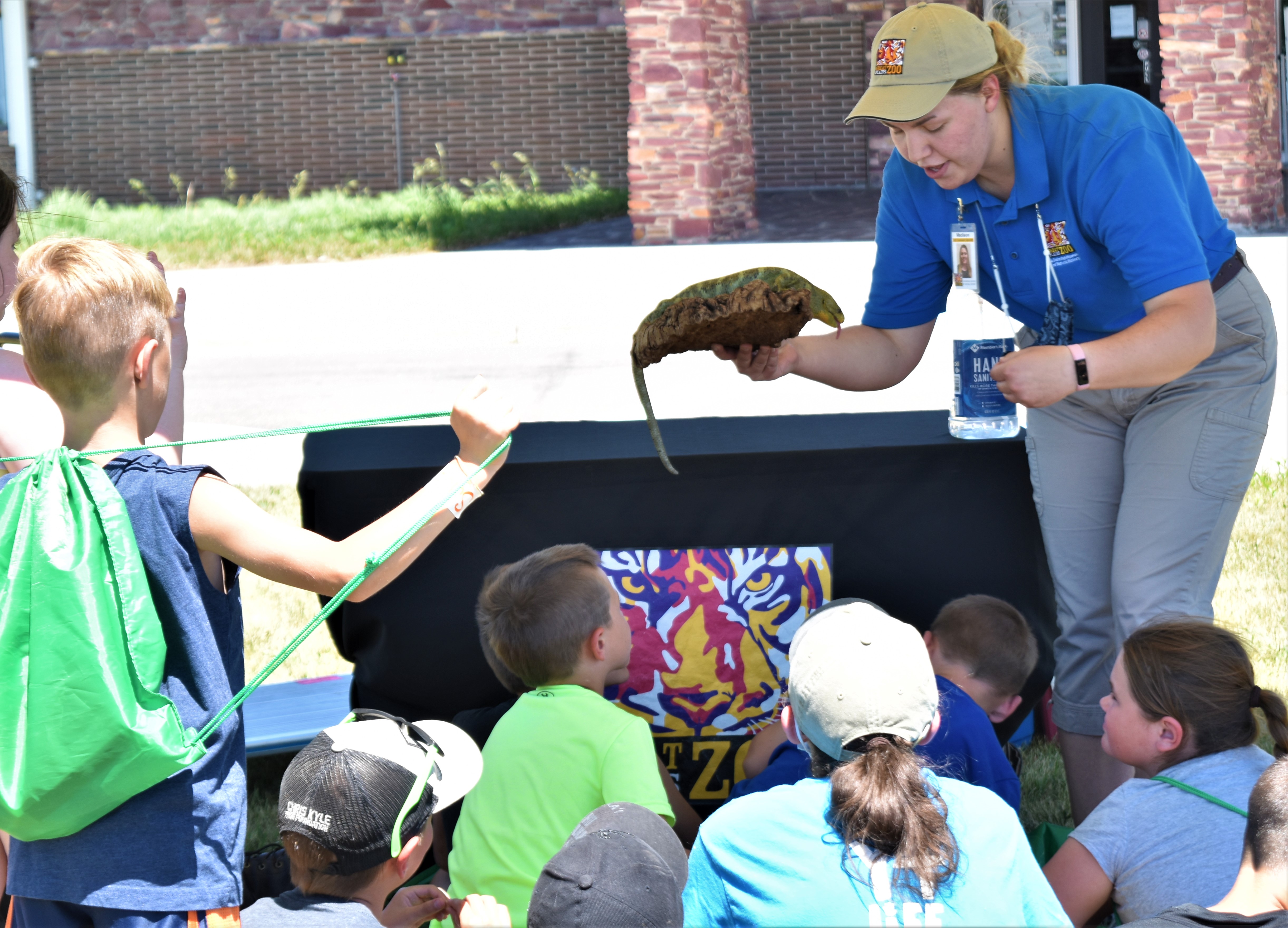A female in holds a reptile for a group of kids to pet outdoors