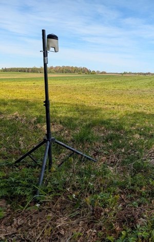 A black tripod sits on grass. At the top of the tripod is a football-sized device used to measure air quality.