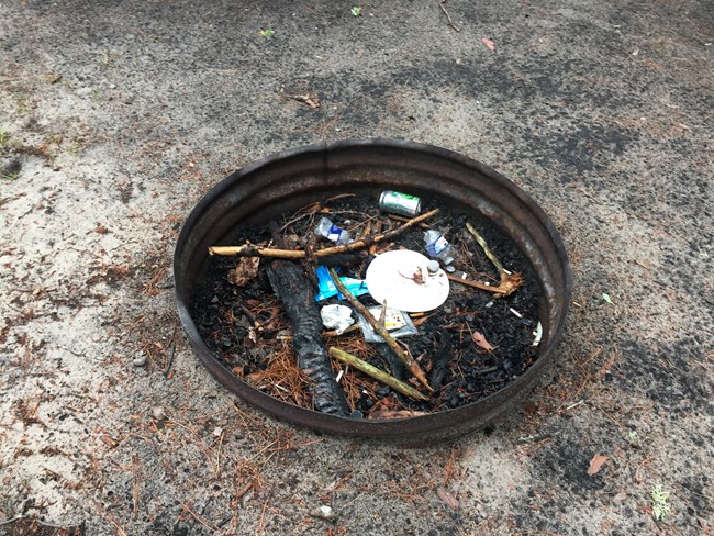 trash left in fire ring amongst charred wood and ash