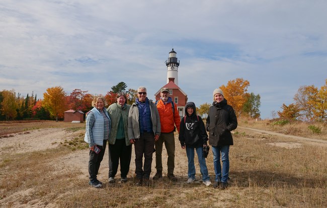 A group of people stand in front of a white lighthouse during autumn