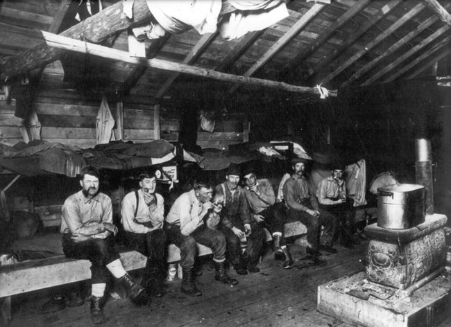 A group of men sit on a long bench in a rustic cabin
