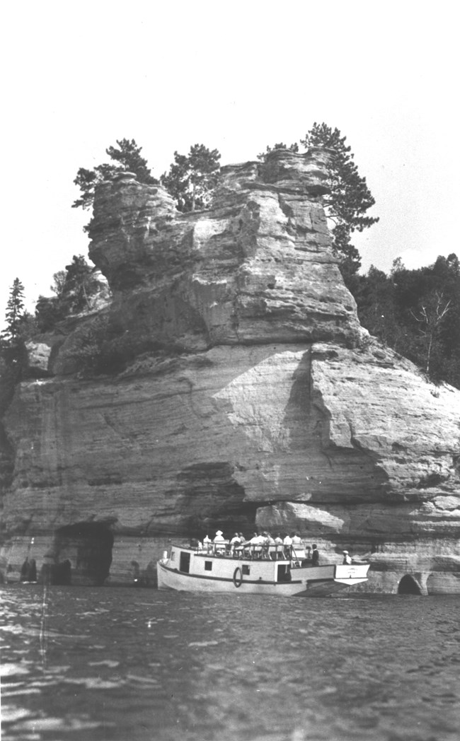 A small boat carries passengers along a cliff