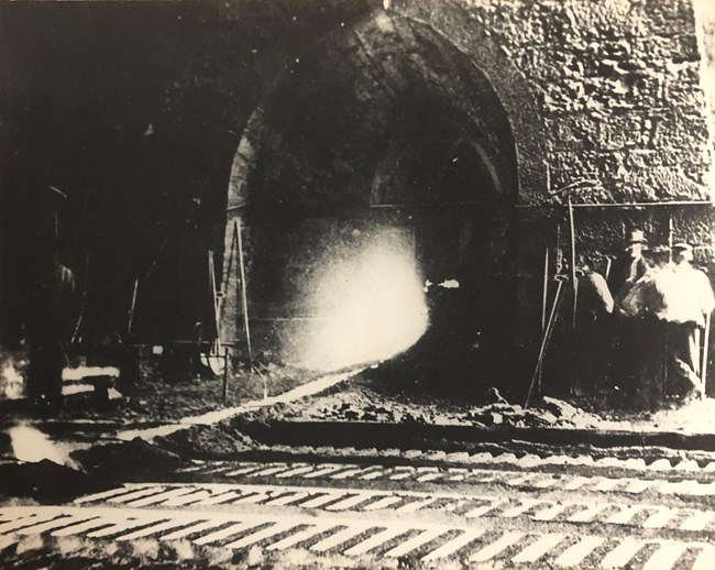 Molten material flows from a large, brick archway and into rectangular molds on the ground.