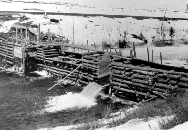 A long dam made of wood stretches across a river