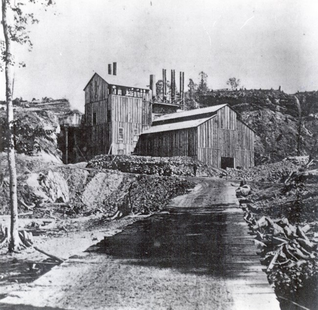 Large wooden building with smokestacks in a barren, logged area.