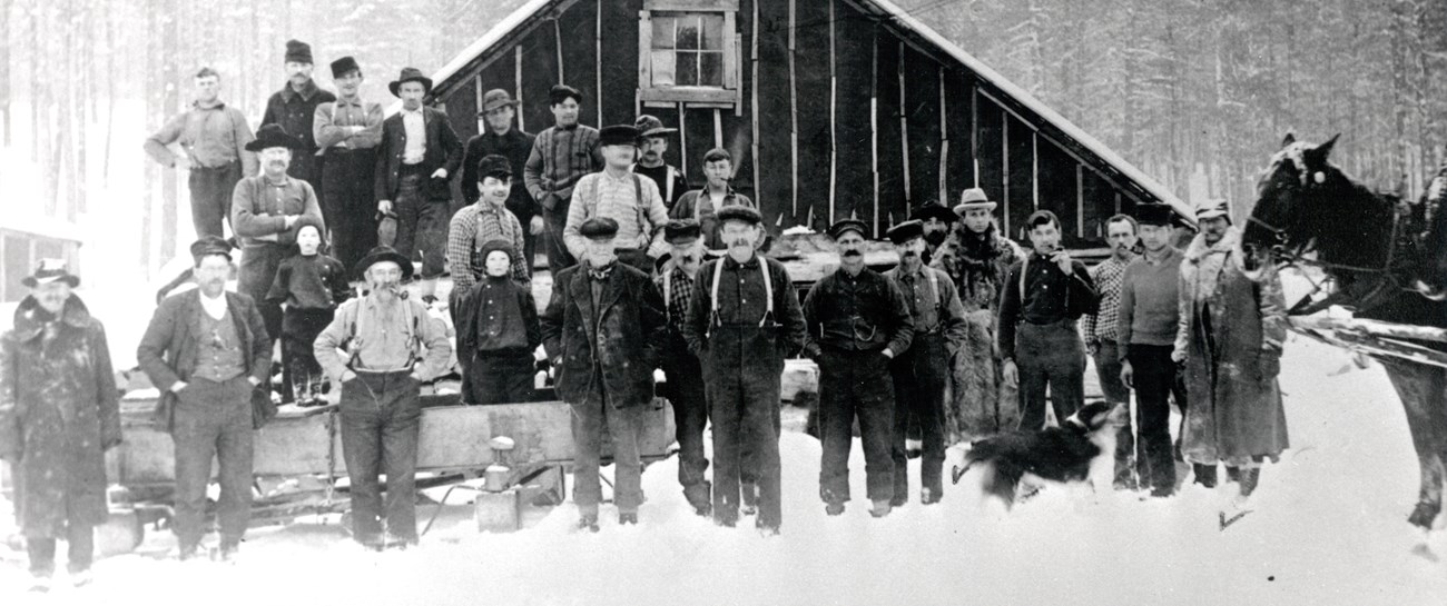 A group of men and a horse stand in front of a very snowy cabin