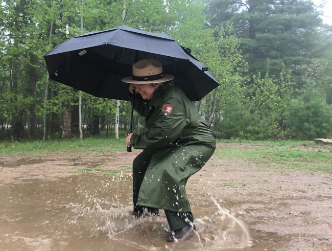 Park Ranger holding an umbrella and jumping in a puddle.