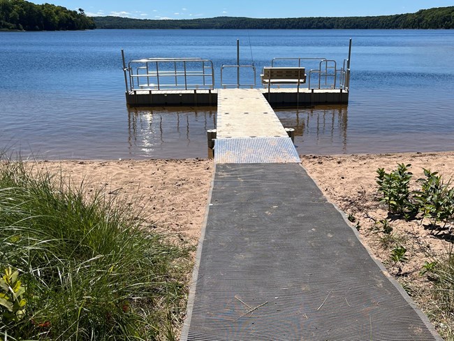 long grey mat leading across beach to metal dock