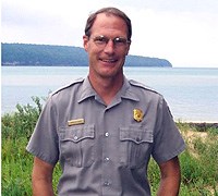 Chris Case, Facility Manager at Pictured Rocks National Lakeshore poses for the camera with Lake Superior in the background.